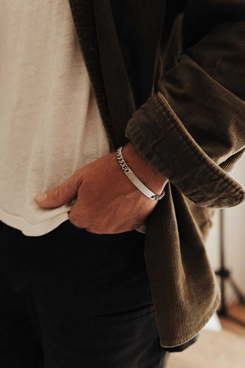 Close up engraving details are shown on man's bracelet as he stands with hand in his pocket.
