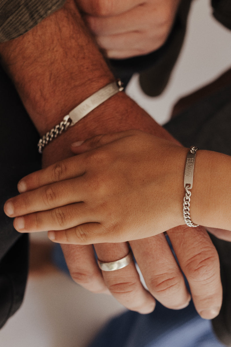 Close-up of two hands with bracelets and a ring on a blurred background. Matching father and son bracelets