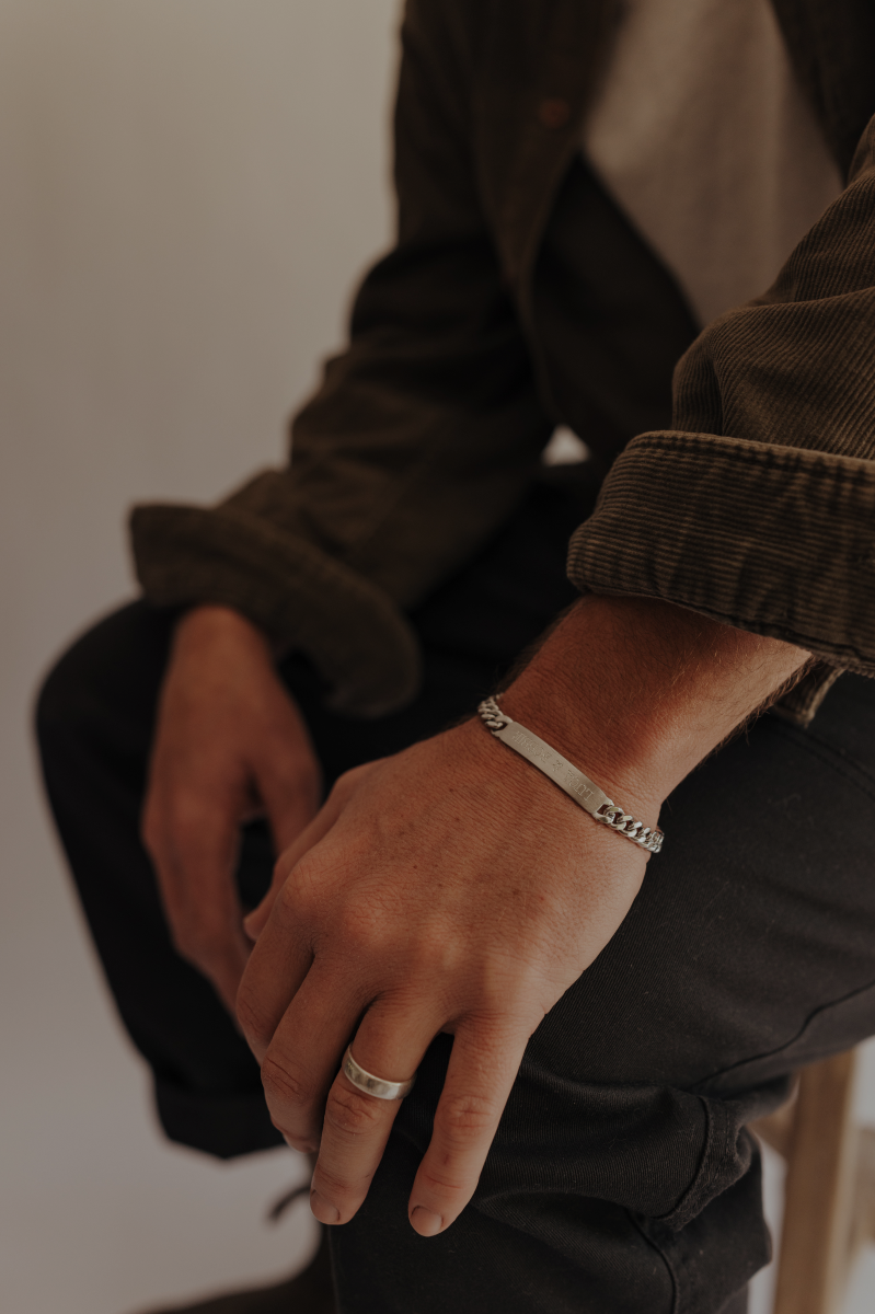 Close-up of a person's hands with a bracelet and ring, wearing a brown jacket.