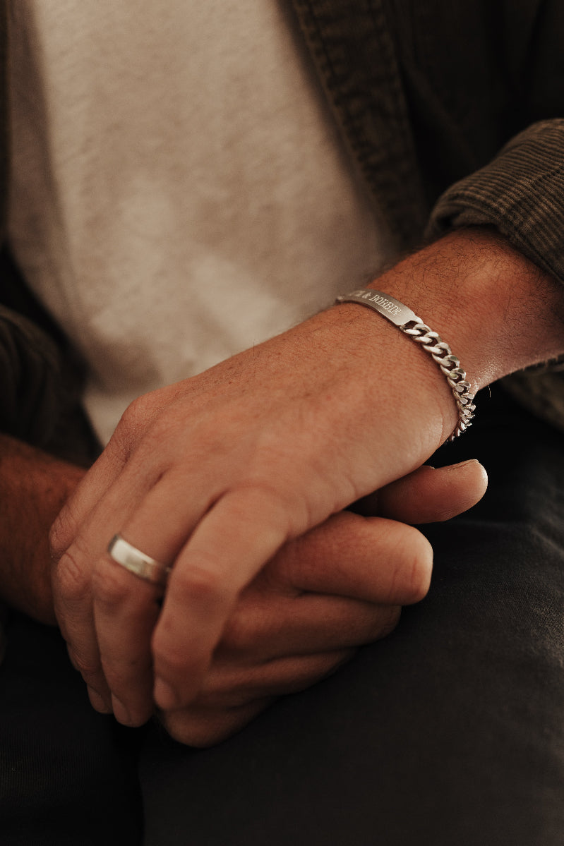 a man has his hands placed one over the other and his bracelet and matching ring showing.