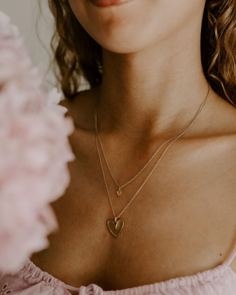 A beautiful side angle of the Petite Darling Necklace worn by a teenage girl. The petite heart shaped pendant rests on a fine cable chain necklace and is a timeless necklace.