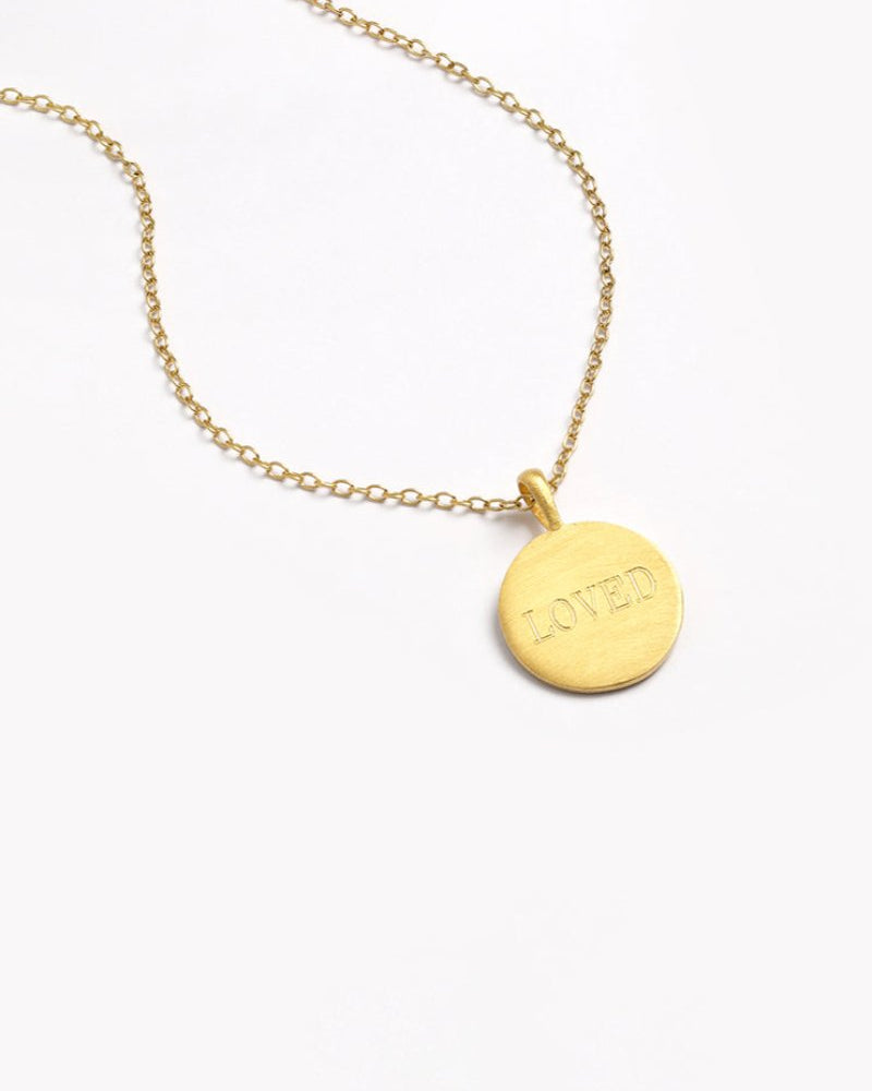 Close-up of engraved gold disc necklace on fine chain, personalised with 'LOVED' text.