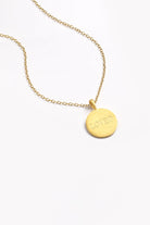 Close-up of engraved gold disc necklace on fine chain, personalised with 'LOVED' text.
