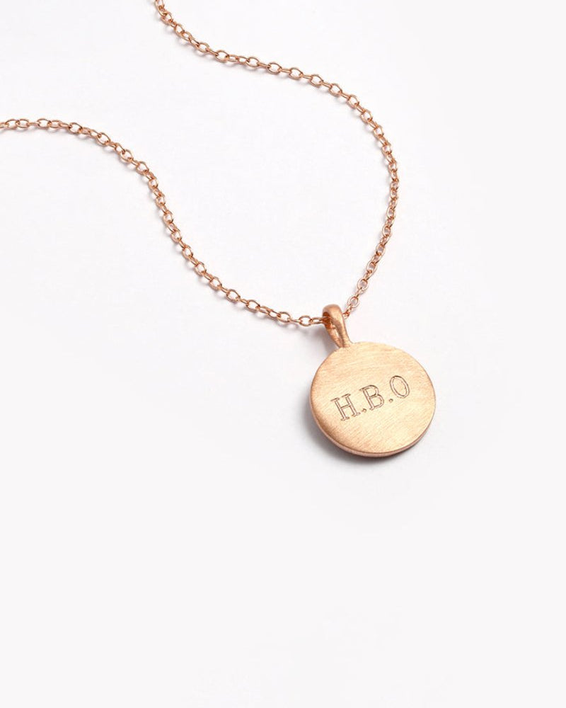 Close-up of Petite Signature Necklace in rose gold with engraved initials on a round pendant and fine chain for everyday wear.