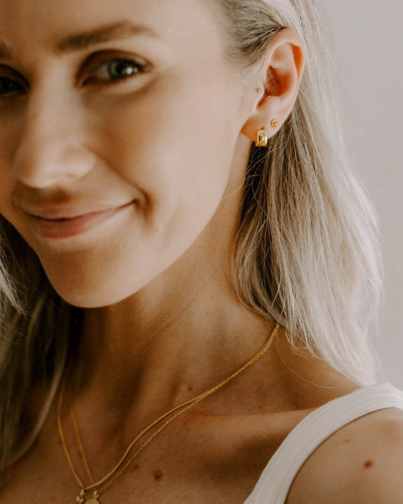 A woman is wearing the Petite Huggie Earrings in her first earring hole and the Petite Daisy Studs in her second hole as a stacked earring look.