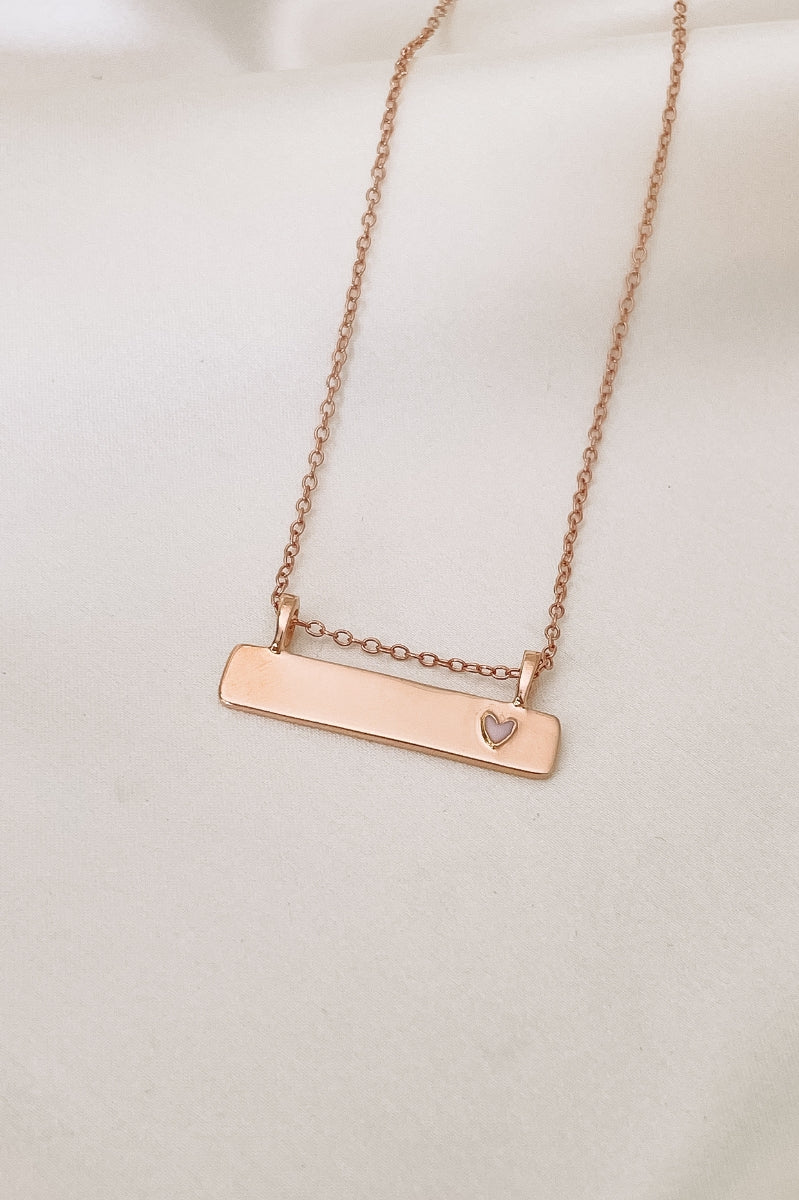 Pink Darling Bar Necklace in rose gold. A smooth bar pendant necklace that is engravable and features a small pink heart at the end of the bar pendant