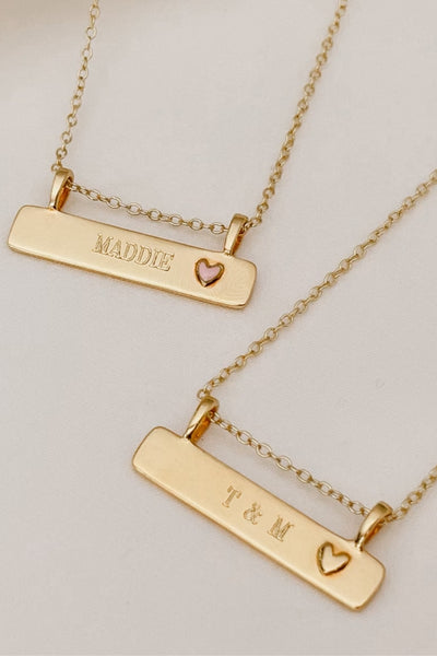 A Pink Darling Bar Necklace sits alongside a Darling Bar Necklace.  Both necklaces have personalised engraving on the front of them.