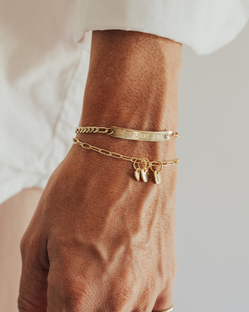 A close-up image of layered gold bracelets, the Posie and Pink Darling, featuring a heart charm and personalised initial pendants, styled as elegant fine jewellery by Bluebird Co