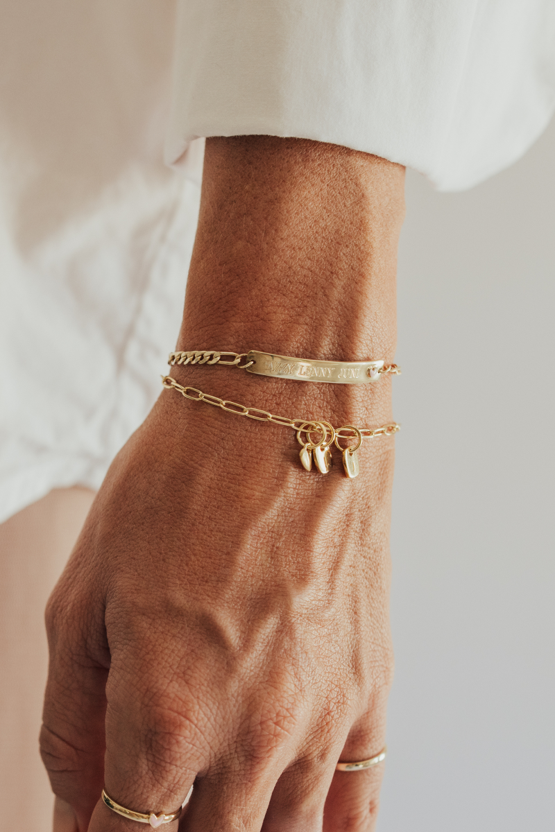 A close-up image of layered gold bracelets, the Posie and Pink Darling, featuring a heart charm and personalised initial pendants, styled as elegant fine jewellery