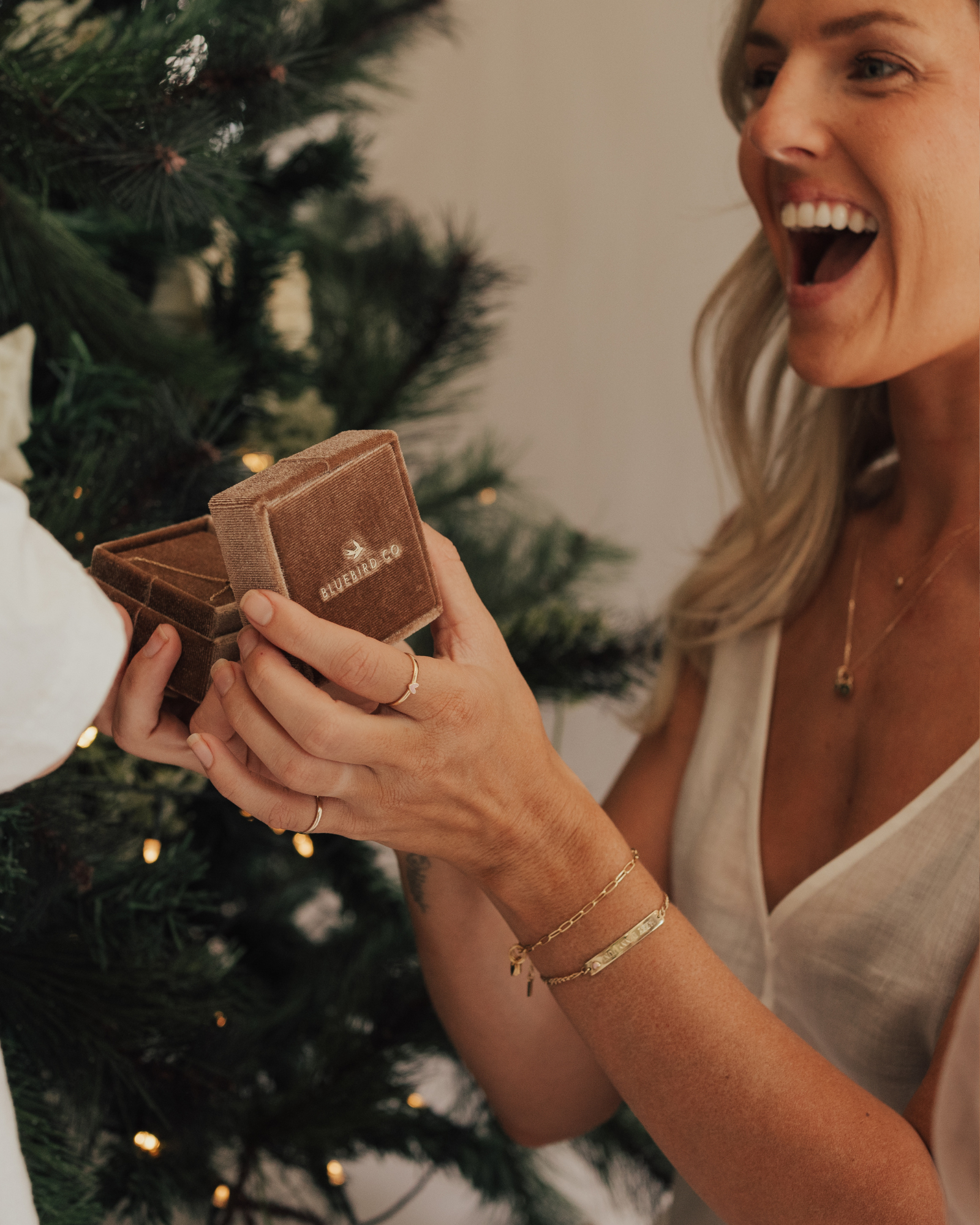 A mother wearing the Posie and Pink Darling bracelets and fine minimalist rings, captured holding a velvet jewellery box and radiating happiness by Bluebird Jewellery.