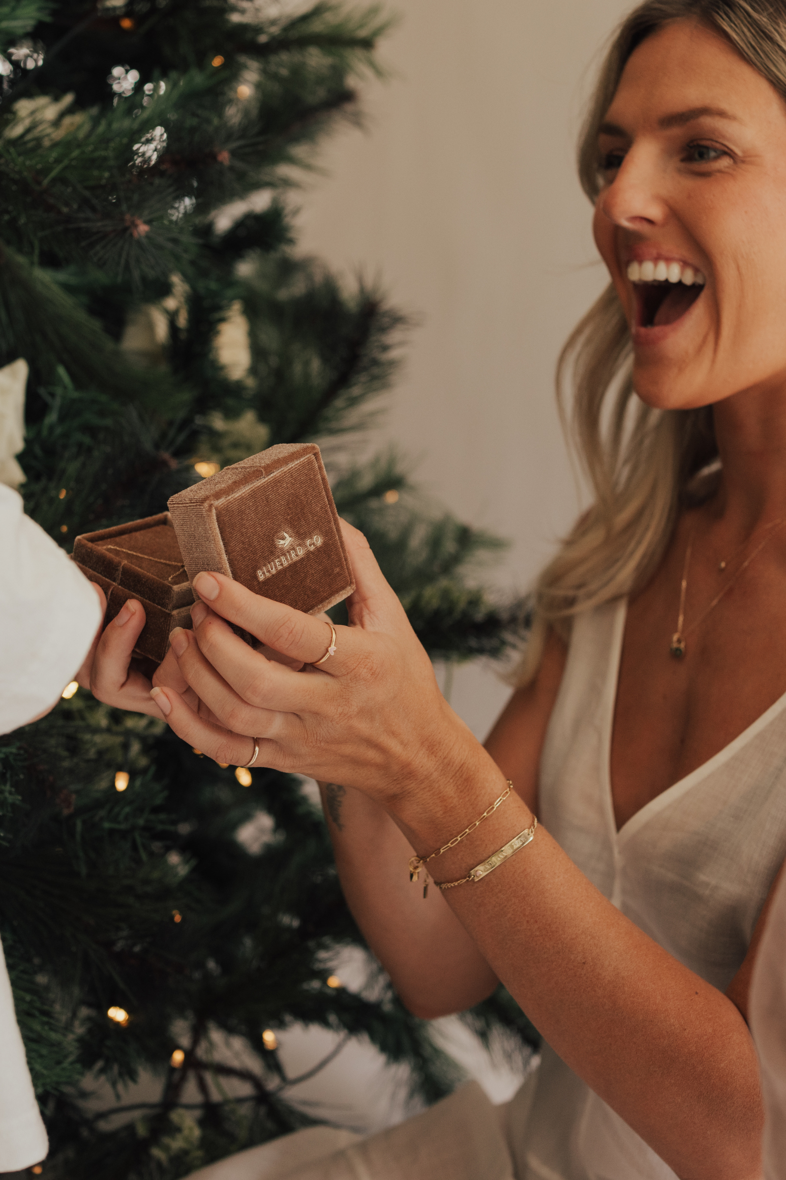 A mother wearing the Posie and Pink Darling bracelets and fine minimalist rings, captured holding a velvet jewellery box and radiating happiness