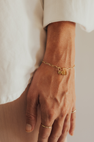 A woman wearing a gold Posie Bracelet with heart charm and engraved rectangular pendants, perfectly paired with a Darling Ring for a timeless look.