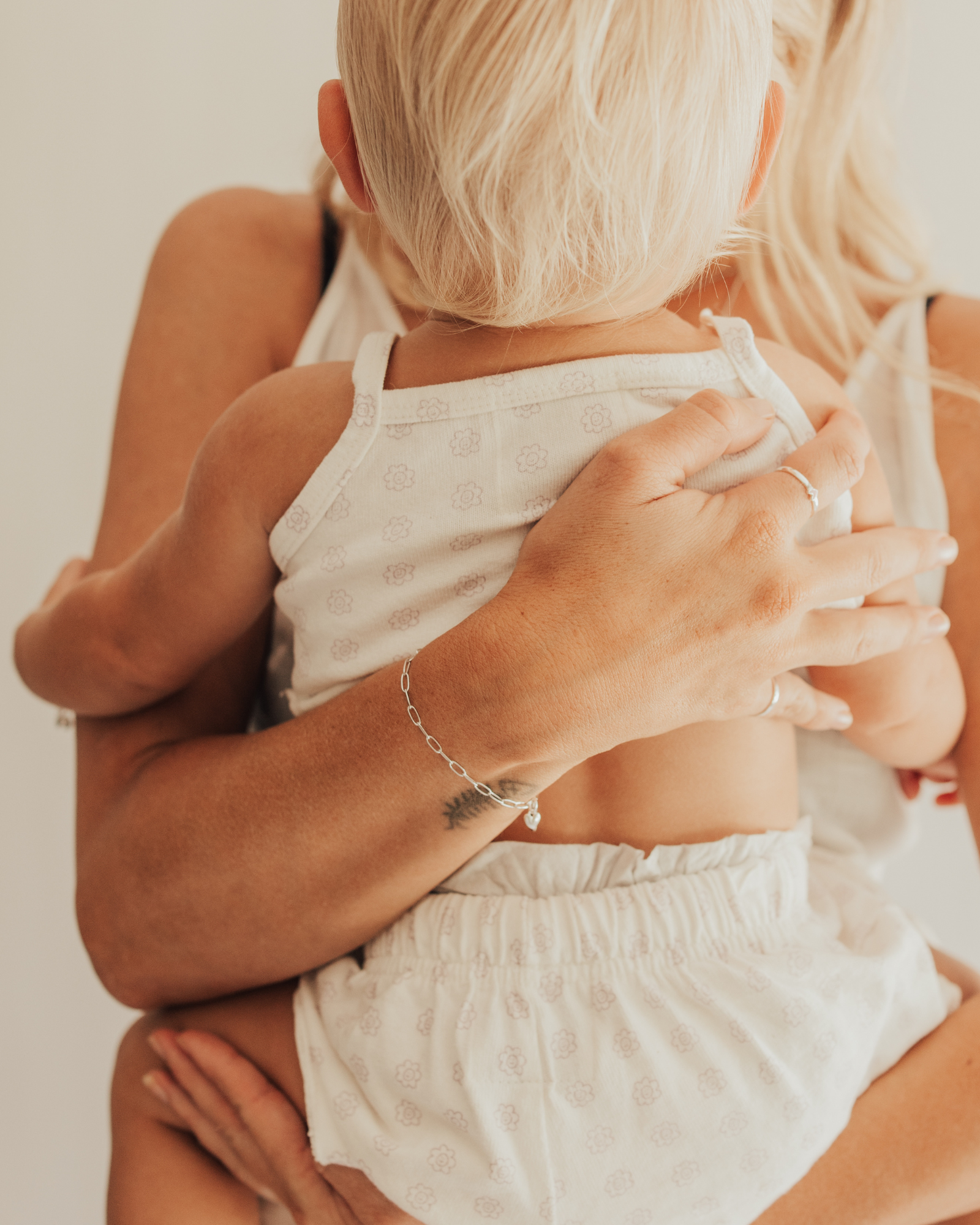 A warm image of a mum and baby wearing matching Posie Bracelets with heart charms by Bluebird Jewellery, captured in a moment of happiness and connection.