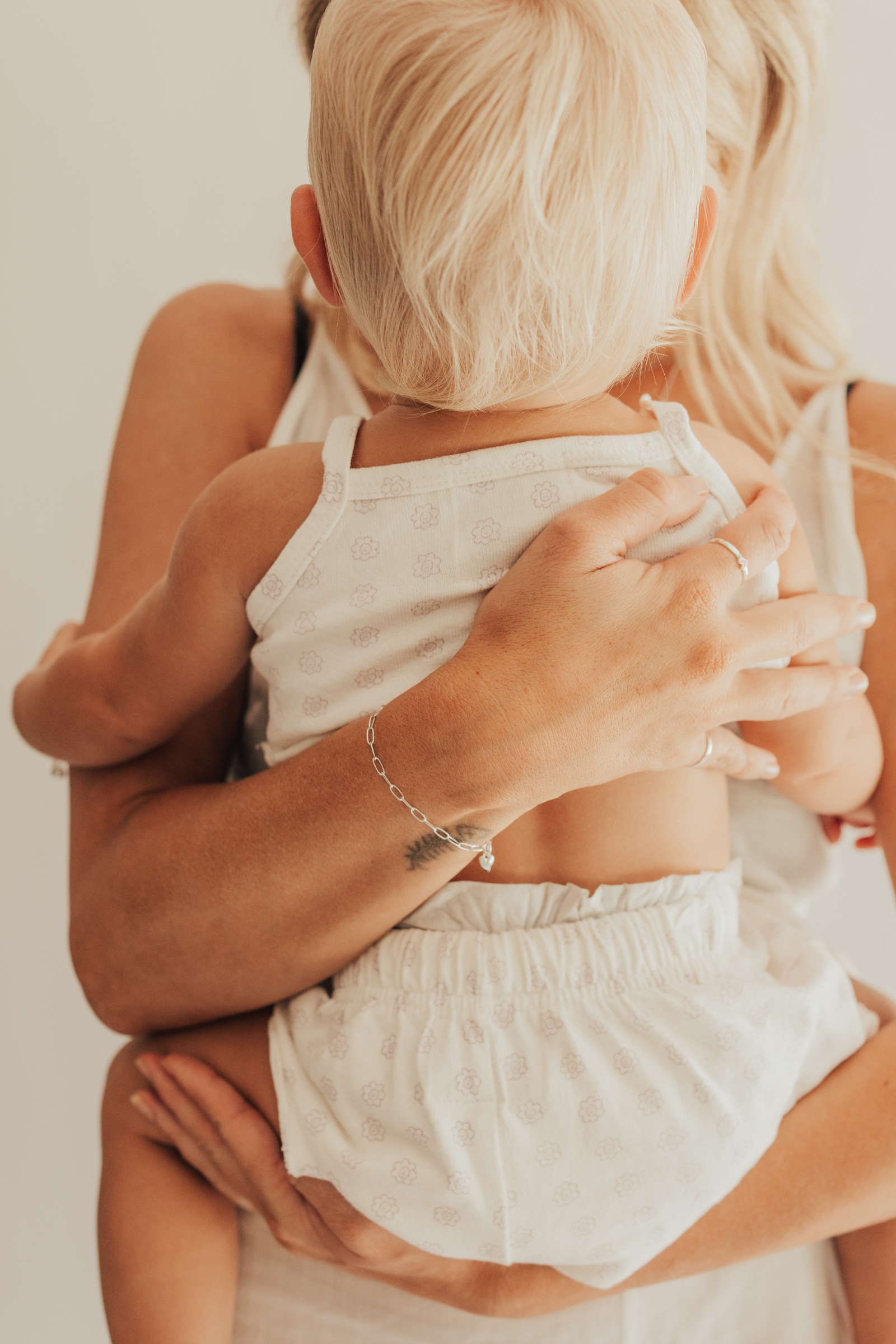 A warm image of a mum and baby wearing matching Posie Bracelets with heart charms, captured in a moment of happiness and connection.