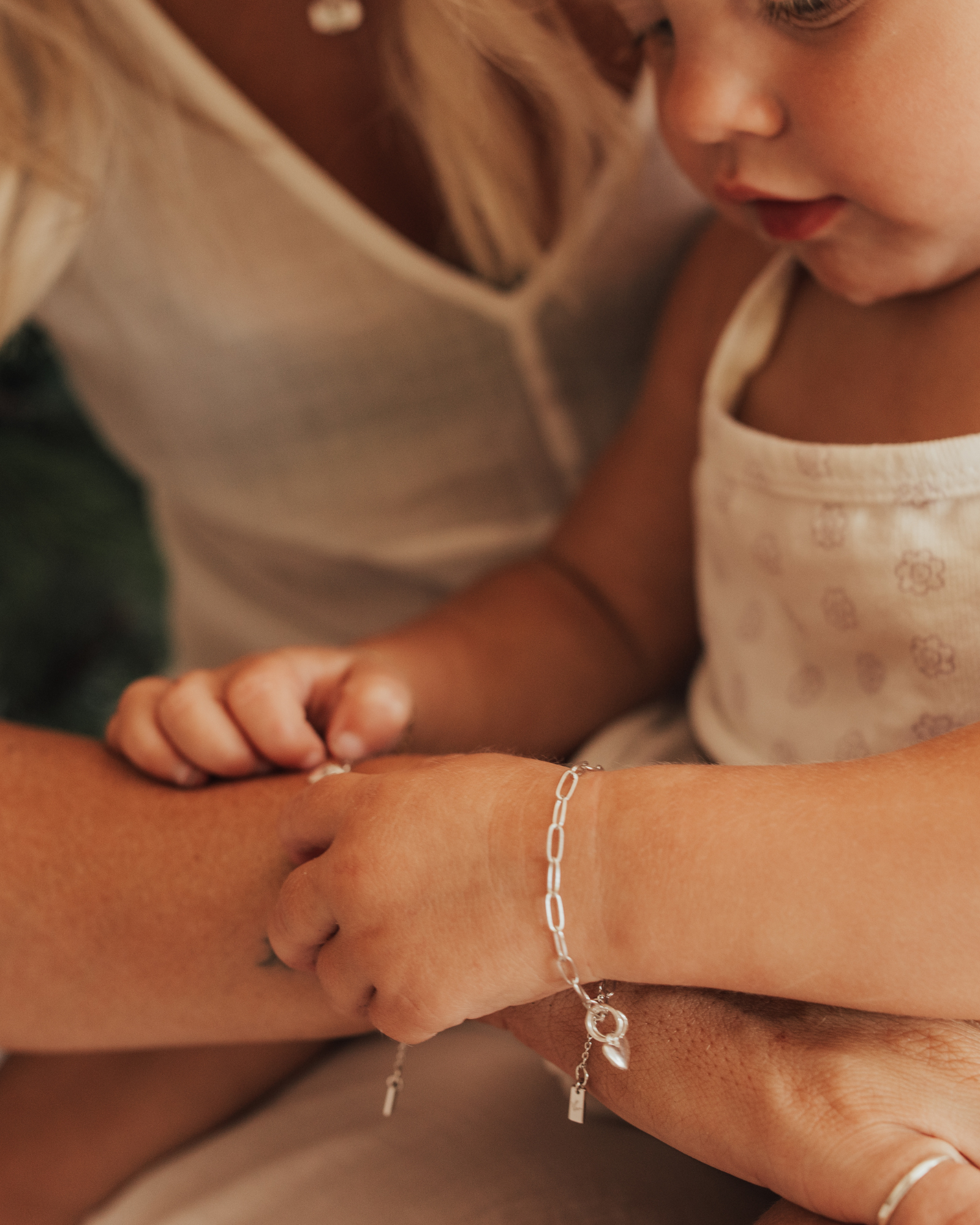 A detailed close-up of a mother and baby wearing the Posie bracelets with heart pendants, captured in natural light to highlight their delicate craftsmanship by Bluebird Jewellery.