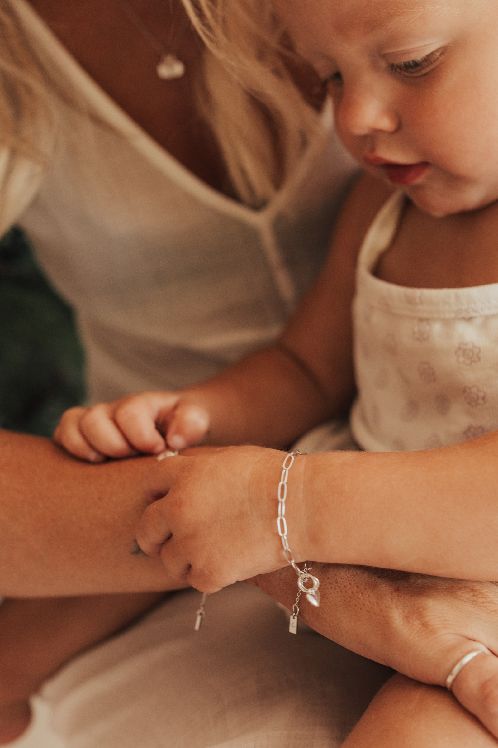 A detailed close-up of a mother and baby wearing the Posie bracelets with heart pendants, captured in natural light to highlight their delicate craftsmanship by Bluebird Jewellery.