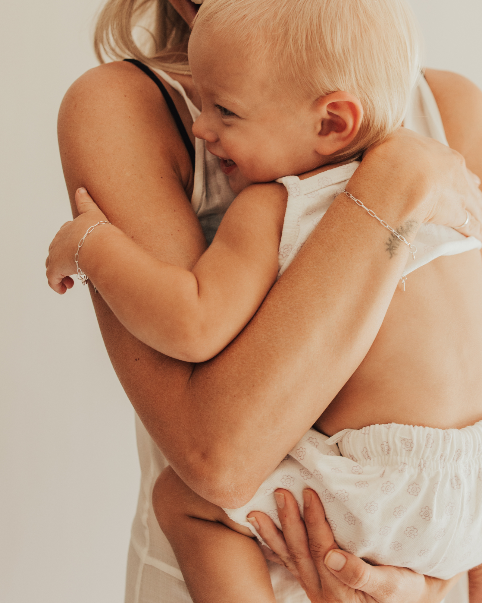 A warm image of a mum and baby wearing matching Posie Bracelets with heart charms by Bluebird Jewellery, captured in a moment of happiness and connection