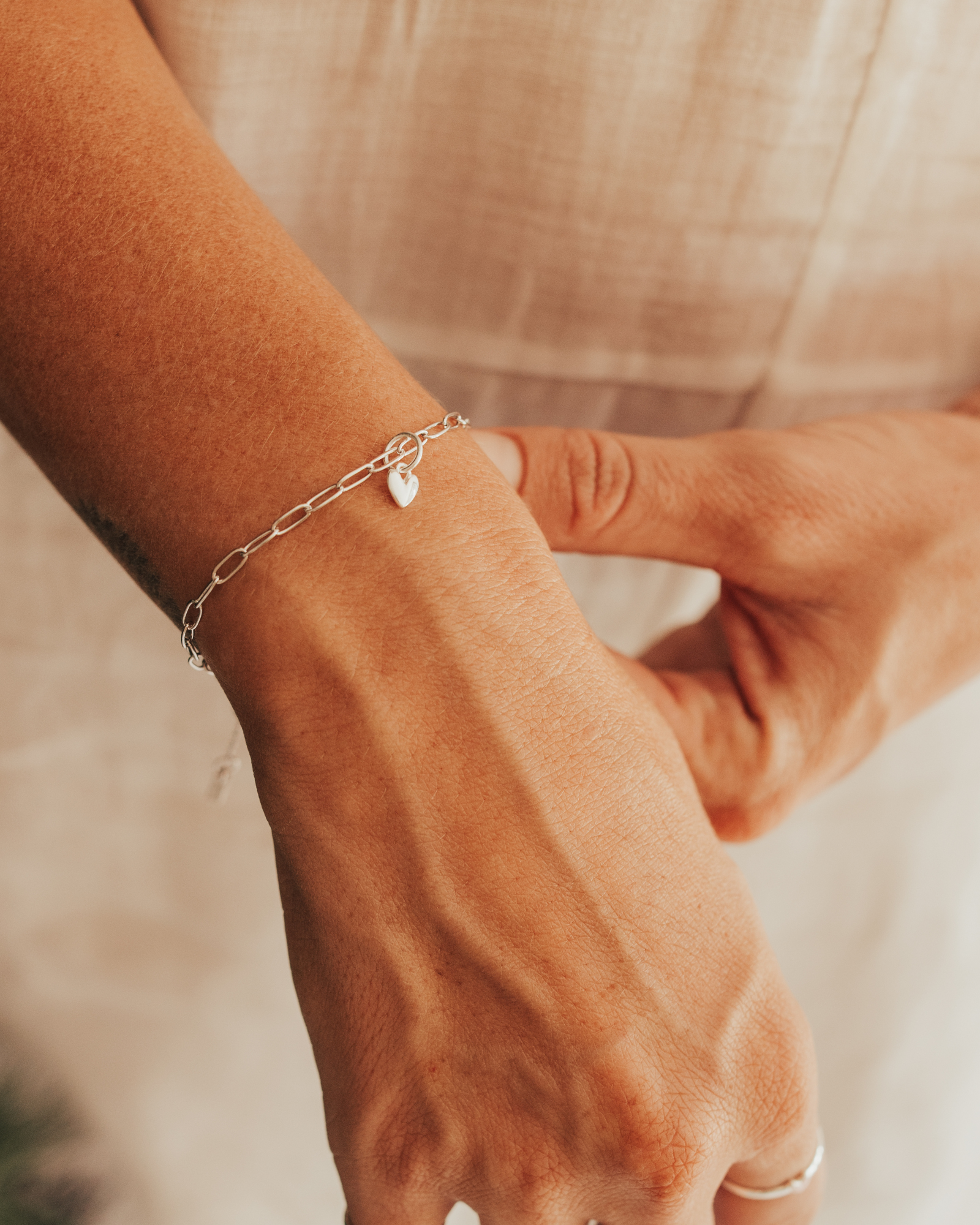 A close-up of a hand wearing a Posie Bracelet with a heart charm, complemented by delicate silver rings for a refined modern finish by Bluebird Jewellery