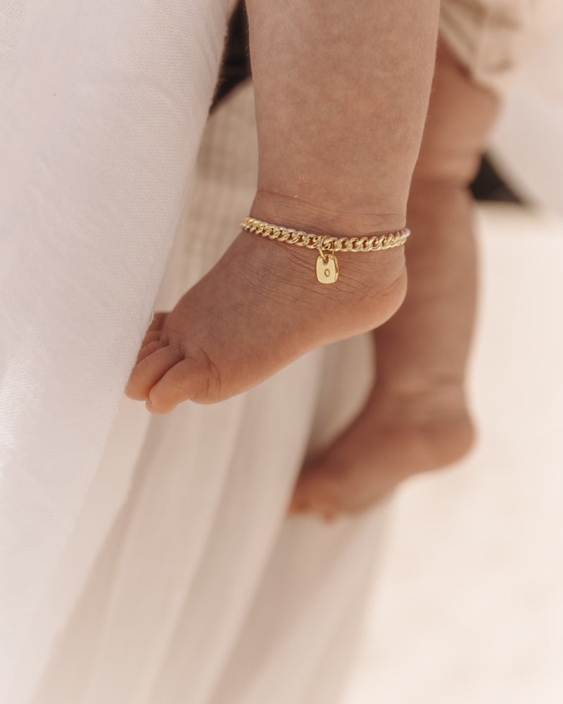 A close-up of a baby’s ankle wearing a gold Cuban Link Chain Bracelet with a rectangular pendant, crafted as a delicate keepsake piece.