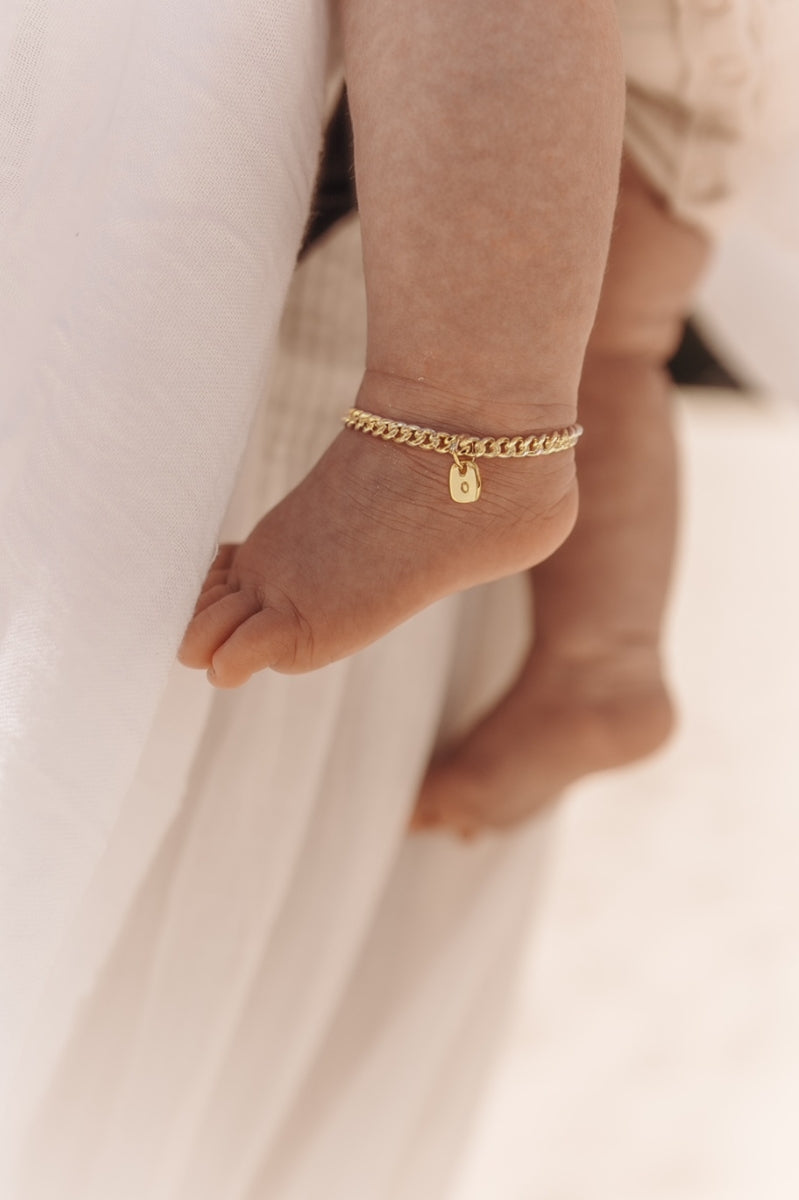 A close-up of a baby’s ankle wearing a gold Cuban Link Chain Bracelet with a rectangular pendant, crafted as a delicate keepsake piece.