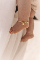 A close-up of a baby’s ankle wearing a gold Cuban Link Chain Bracelet with a rectangular pendant, crafted as a delicate keepsake piece.