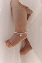 A close-up of a baby’s ankle wearing a silver Cuban Link Chain Bracelet with a rectangular pendant, crafted as a delicate keepsake piece.