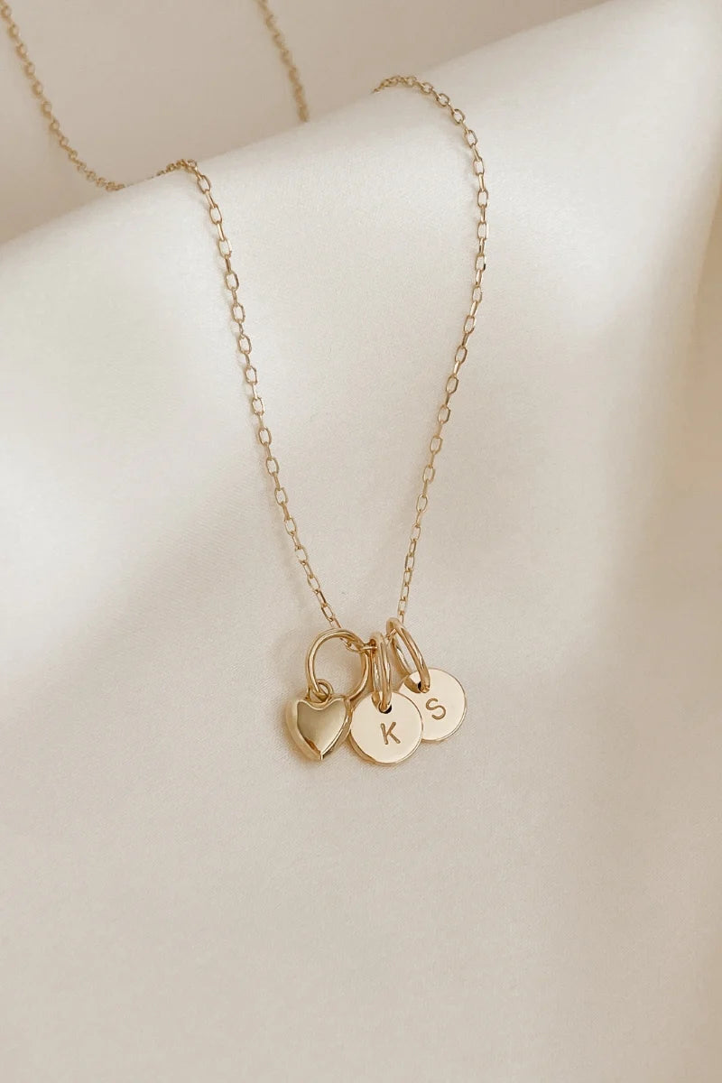 A solid gold necklace chain with petite initial pendants and a solid gold heart pendant