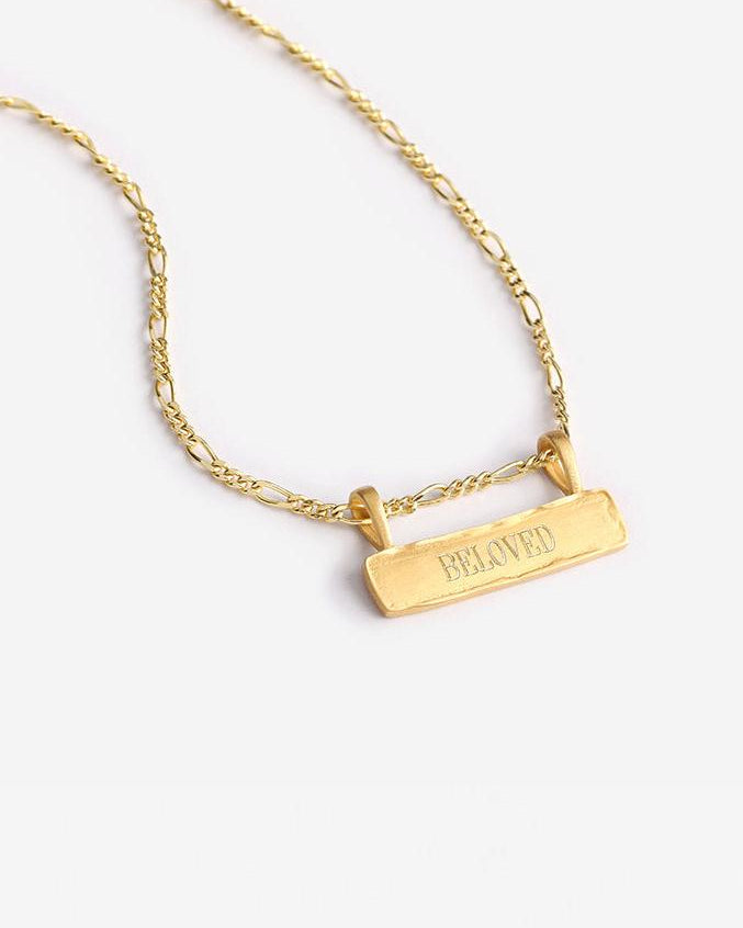 a Signature Bar Necklace with the word BELOVED engraved on the front of the bar pendant. The necklace features a figaro necklace chain and a raised, textured edge on the bar pendant.