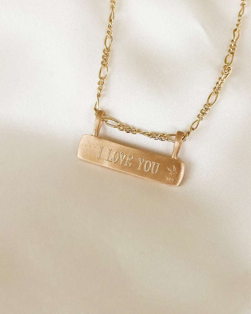 Engraved gold bar necklace with “I LOVE YOU” message, featuring figaro chain, a meaningful everyday keepsake.