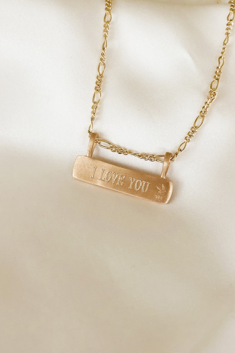 Engraved gold bar necklace with “I LOVE YOU” message, featuring figaro chain, a meaningful everyday keepsake.
