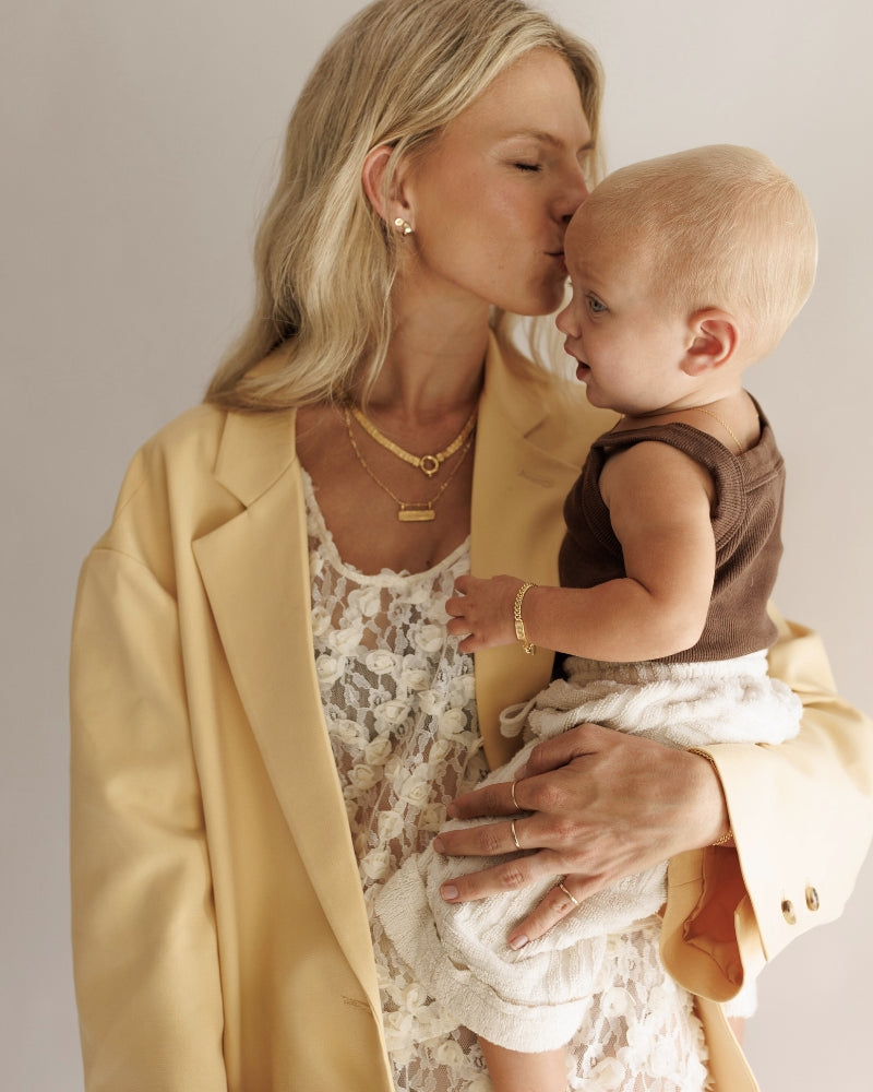 A long image of a mother kid=ssing her daughter's head. The mother is wearing matching Bluebird Co jewellery to her daughter and the jewellery is all personalised.