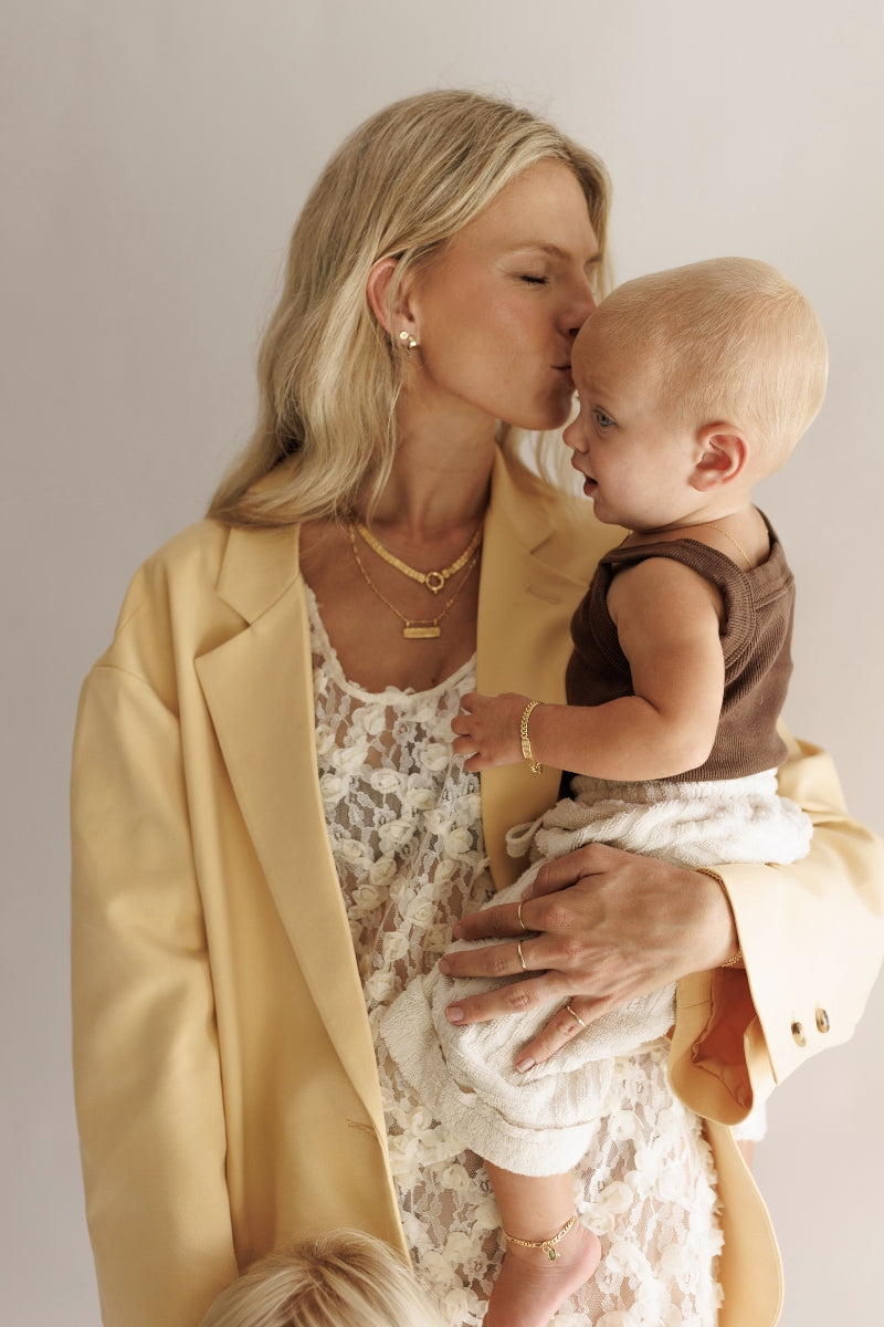 A long image of a mother kid=ssing her daughter's head. The mother is wearing matching Bluebird Co jewellery to her daughter and the jewellery is all personalised.