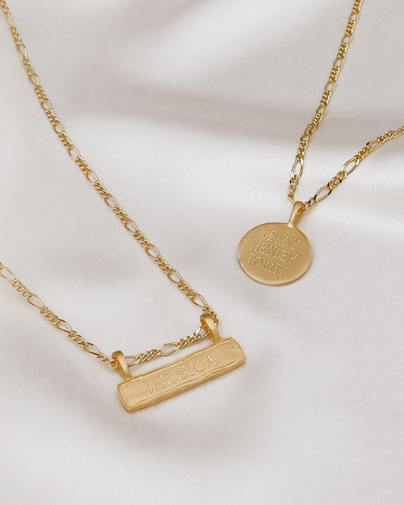 A Signature Bar Necklace and Signature Necklace are laying together on a silk backdrop. Both necklaces feature personalised engraving.