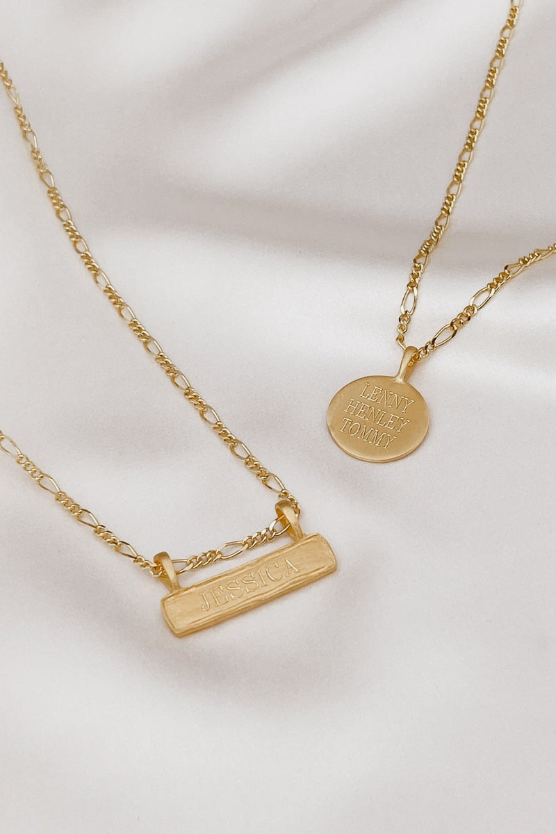 A Signature Bar Necklace and Signature Necklace are laying together on a silk backdrop. Both necklaces feature personalised engraving.