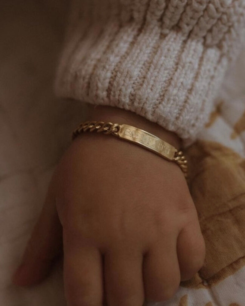 A baby is wearing a Baby sized Signature Bracelet with personalised engraving on it by Bluebird Jewellery.