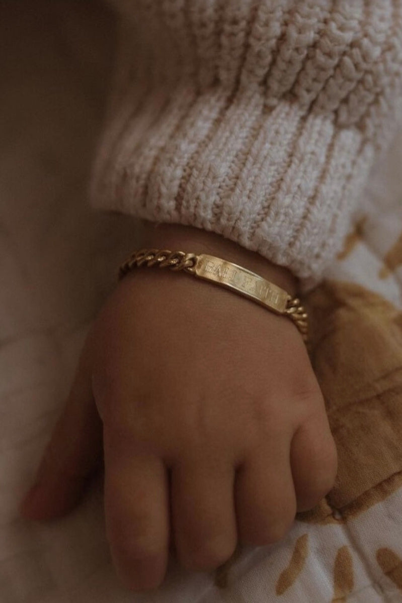 A baby is wearing a Baby sized Signature Bracelet with personalised engraving on it by Bluebird Jewellery.