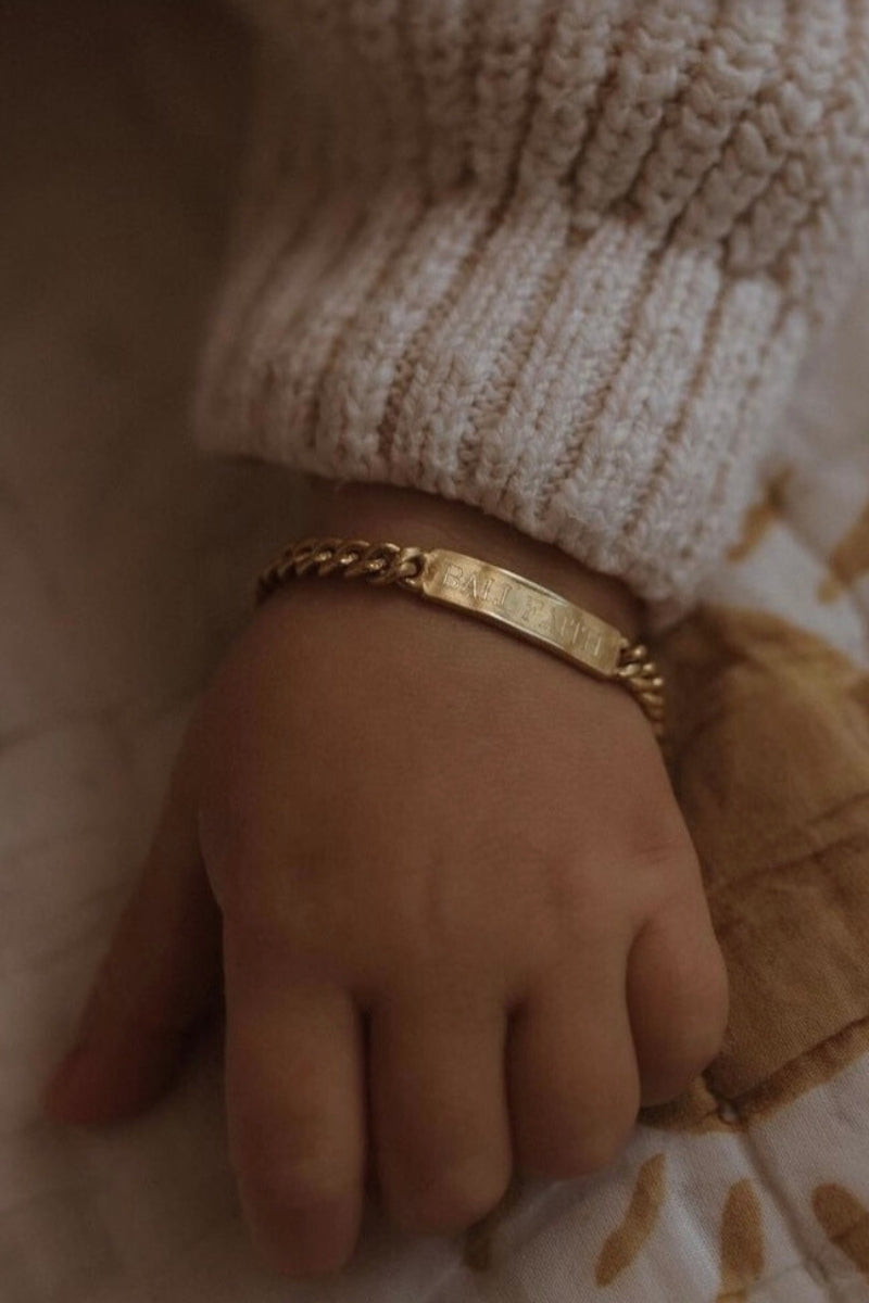 A baby is wearing a Baby sized Signature Bracelet with personalised engraving on it by Bluebird Jewellery.