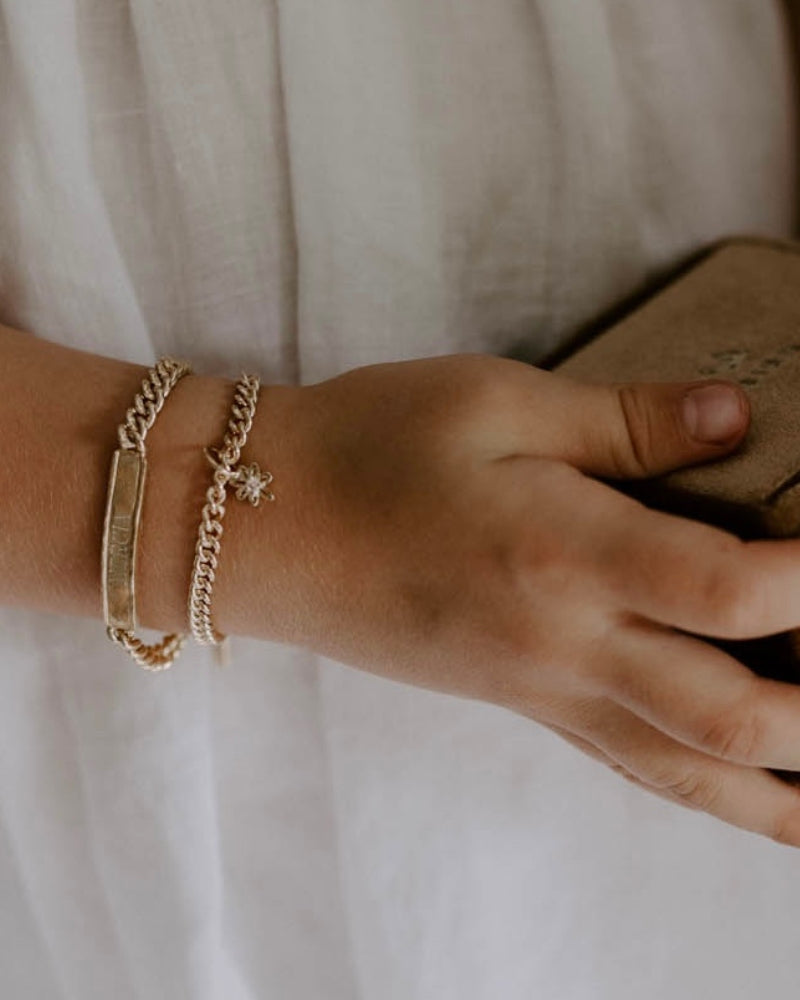 Child wearing engraved gold bracelet and charm bracelet, a meaningful keepsake jewellery piece by Bluebird Jewellery.