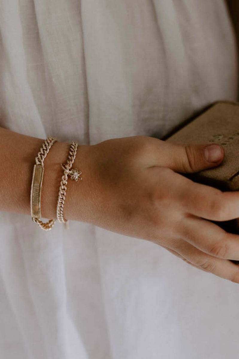 Child wearing engraved gold bracelet and charm bracelet, a meaningful keepsake jewellery piece by Bluebird Jewellery.