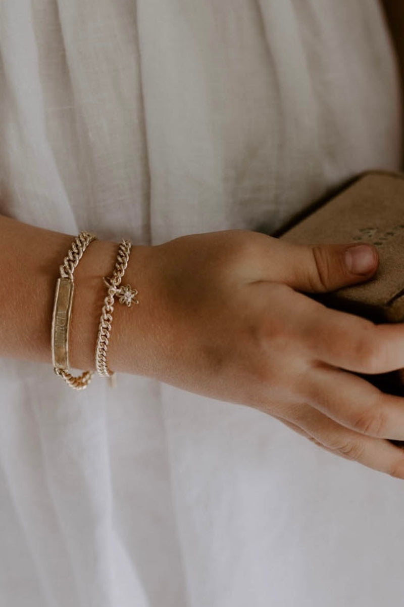 Child wearing engraved gold bracelet and charm bracelet, a meaningful keepsake jewellery piece by Bluebird Jewellery.