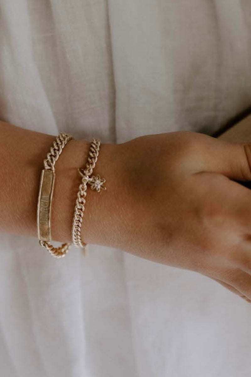 A close-up of a wrist adorned with multiple personalised gold bracelets with a daisy charm designed for everyday wear