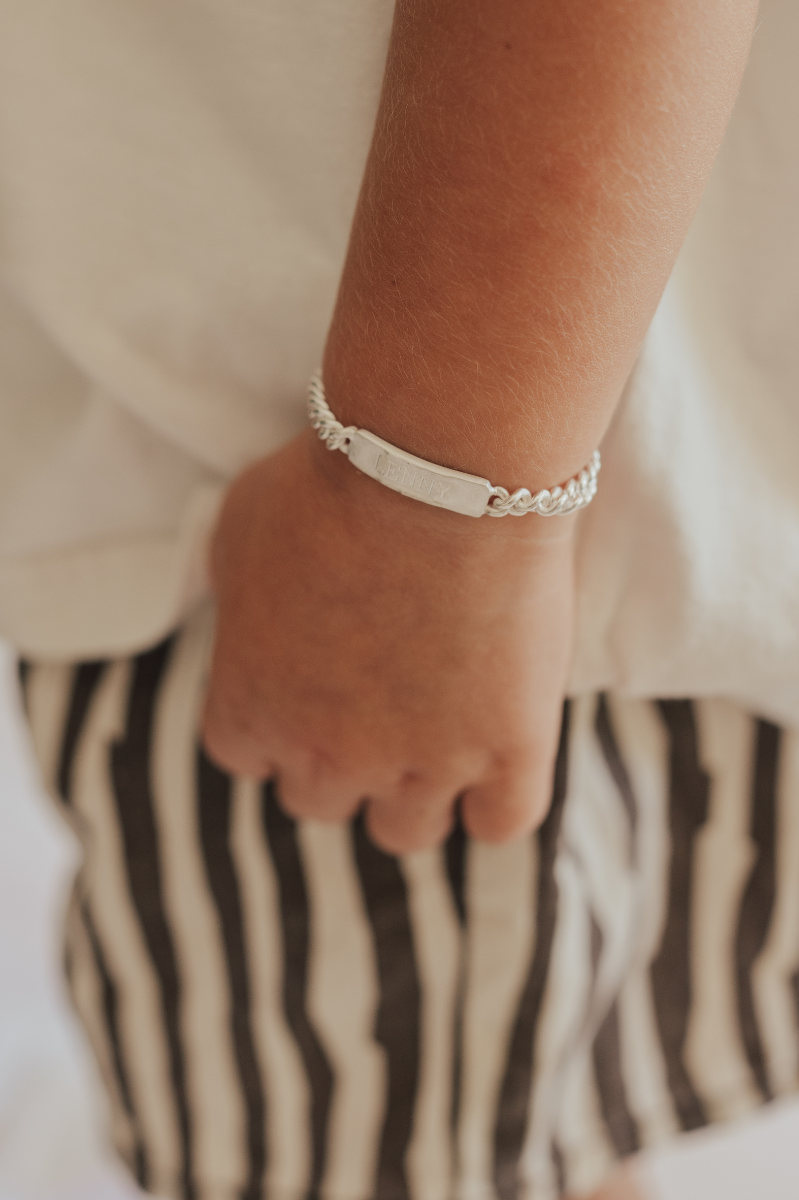 A close up image of a silver signature bracelet being worn by a young boy.  The bracelet features personalised engraving on the front of the bar pendant.