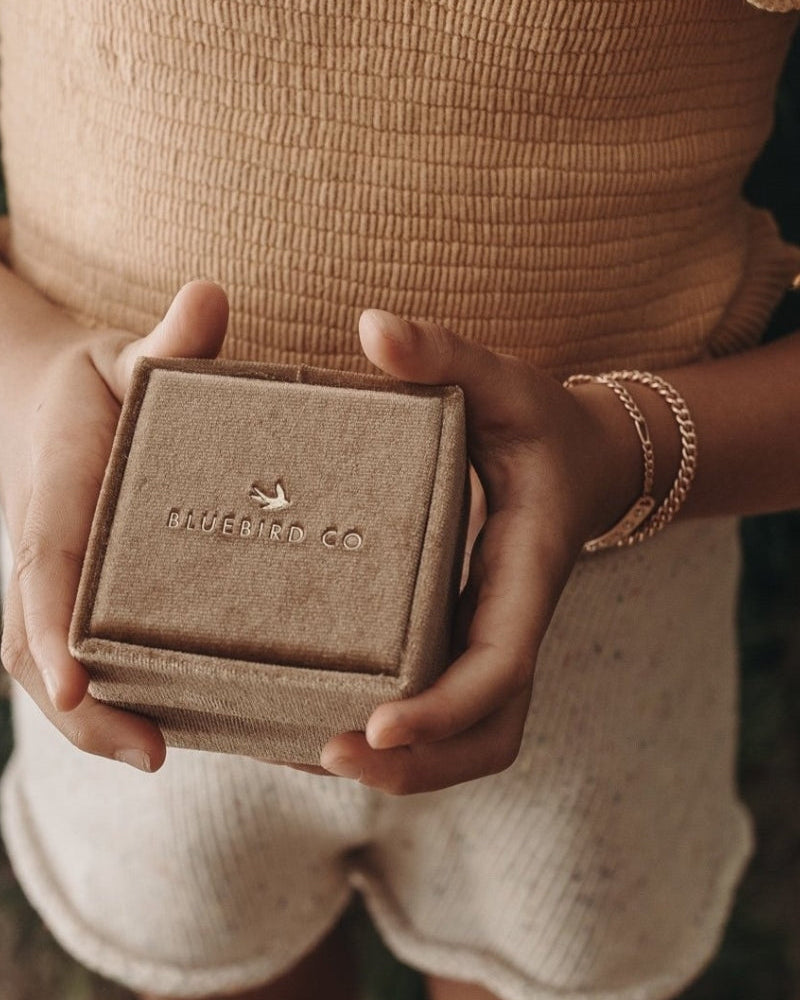 A detailed image of a young child wearing a Cuban Link Chain Necklace with a vintage pearl pendant and matching pearl bracelet while holding a Bluebird Co velvet box, designed as a timeless keepsake by Bluebird Jewellery.