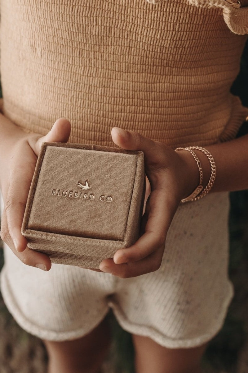 A detailed image of a young child wearing a Cuban Link Chain Necklace with a vintage pearl pendant and matching pearl bracelet while holding a Bluebird Co velvet box, designed as a timeless keepsake.