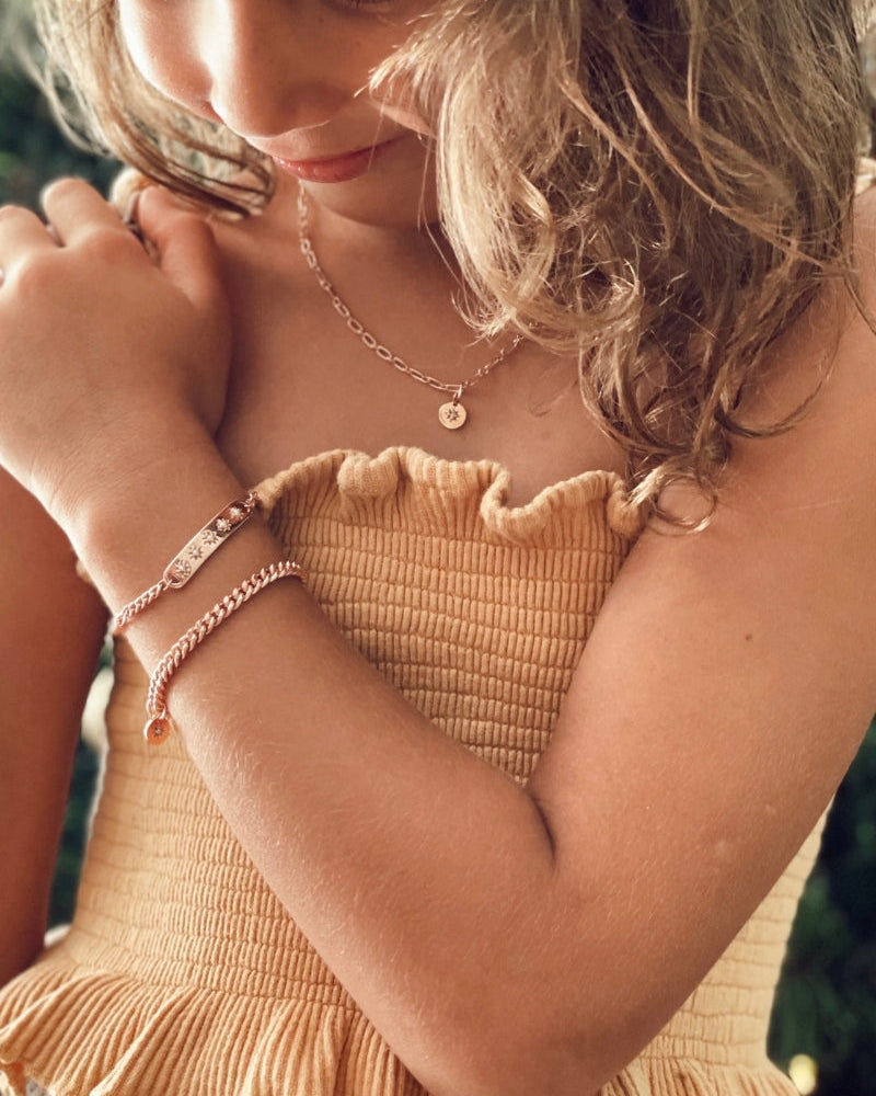 A young child wearing a rose gold Cuban Link Chain with a vintage pearl pendant and matching pearl bracelet, crafted as timeless fine jewellery by Bluebird Co