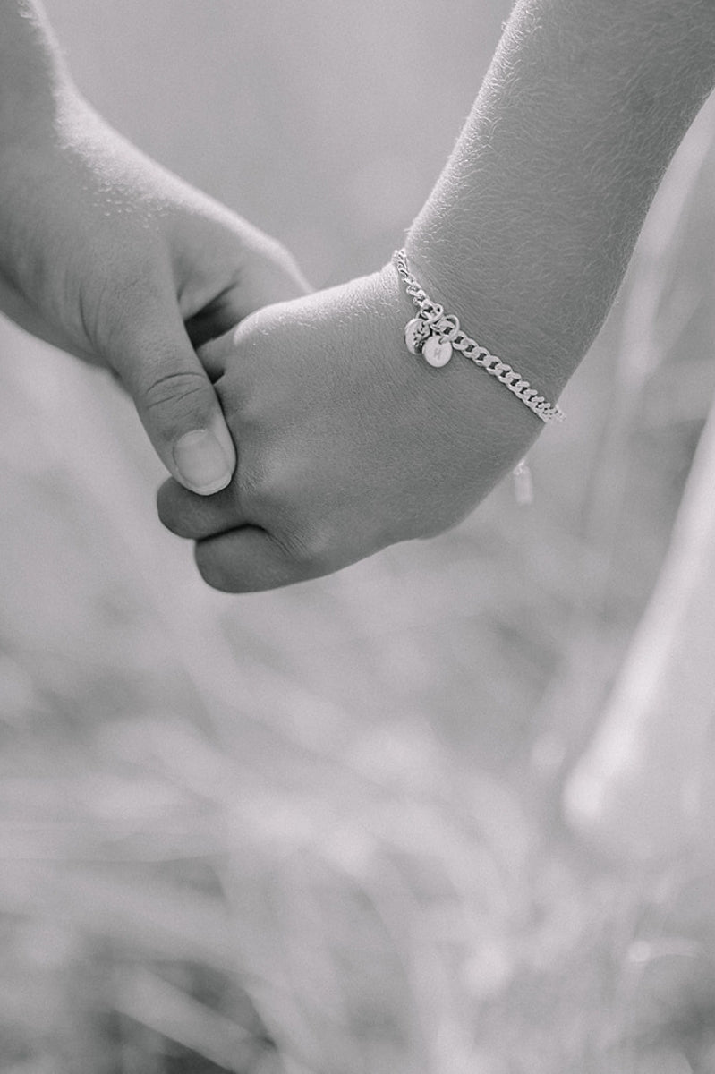 A close up image of a child's wrist wearing a Cuban Link Chain with a single vintage pearl pendant with a personalised solid gold initial pendant, crafted in elegant fine jewellery