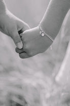 A close up image of a child's wrist wearing a Cuban Link Chain with a single vintage pearl pendant with a personalised solid gold initial pendant, crafted in elegant fine jewellery