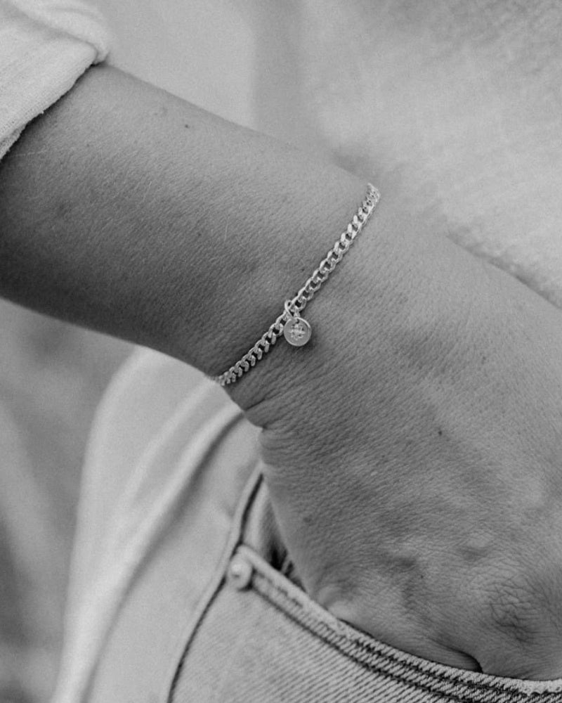 A close up image of a woman's wrist wearing a Cuban Link Chain with a single vintage pearl pendant, crafted in elegant fine jewellery