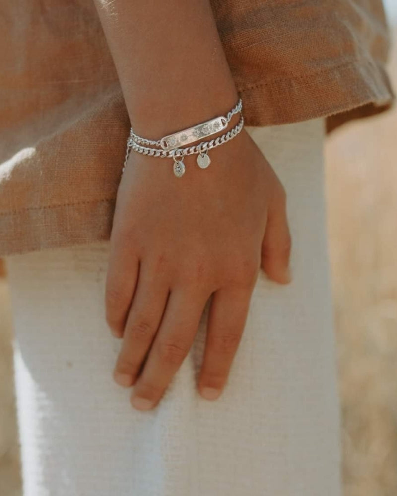 A detailed image of a young child's wrist wearing a Cuban Link Chain Necklace with a vintage pearl pendant and matching pearl bracelet, designed as a timeless keepsake.