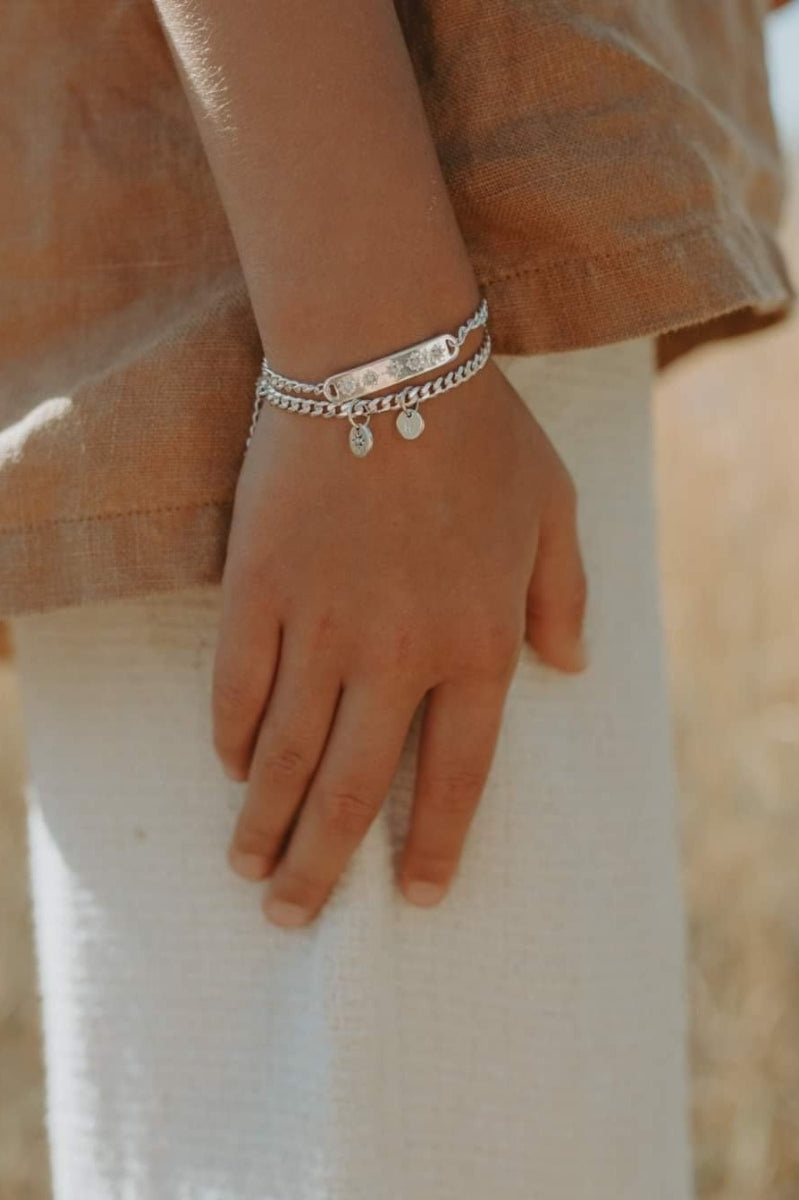 A detailed image of a young child's wrist wearing a Cuban Link Chain Necklace with a vintage pearl pendant and matching pearl bracelet, designed as a timeless keepsake.
